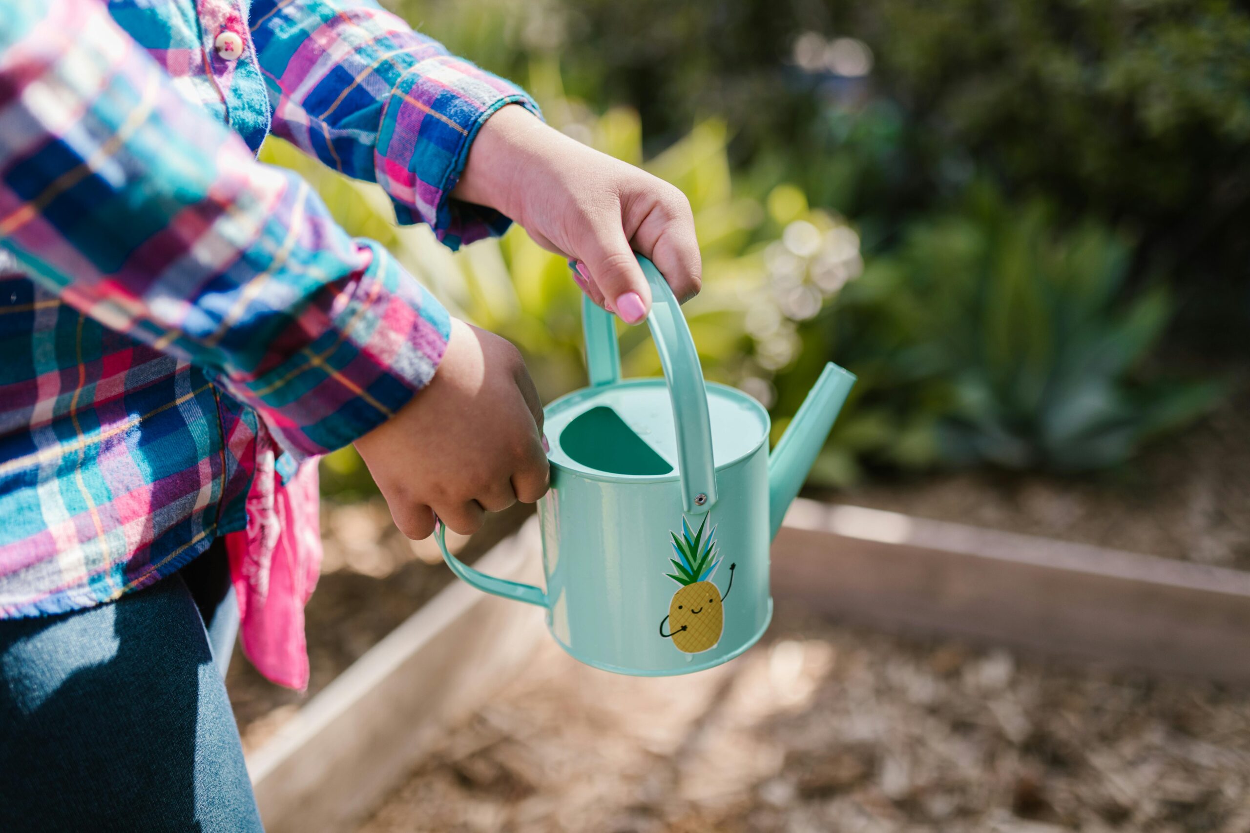 A child enjoys gardening on a sunny day with a playful pineapple watering can.